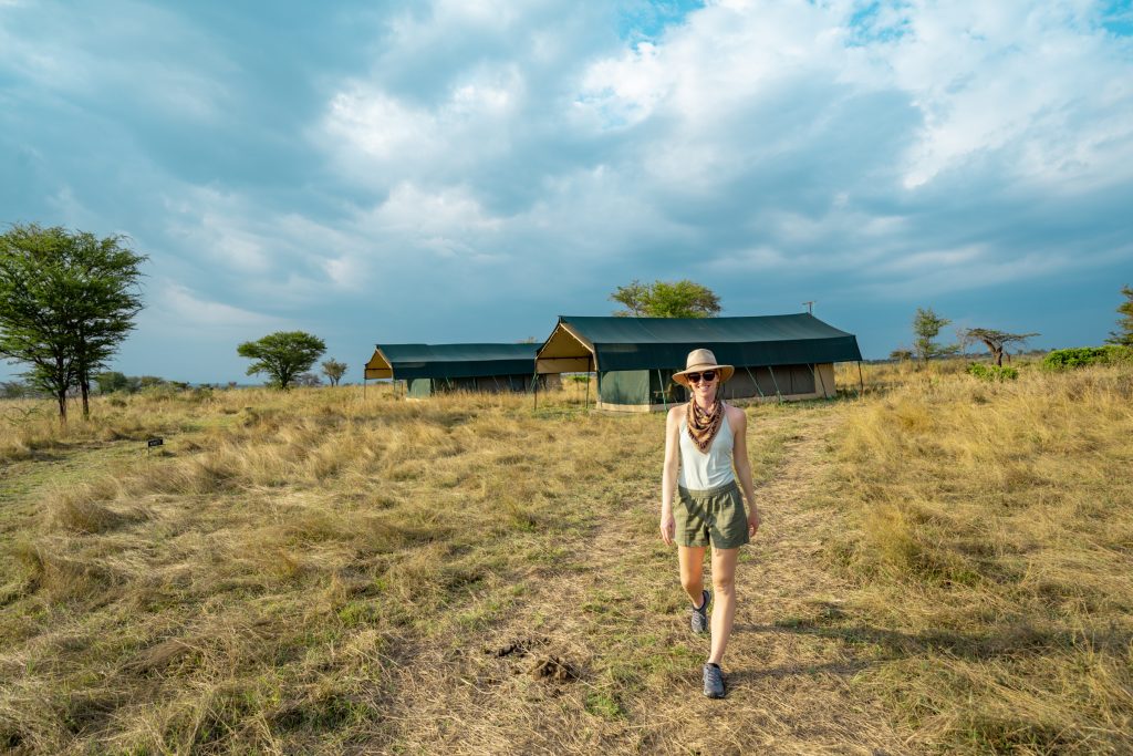 Safari outfit for women around camp: olive green shorts, light green tank, trail runners, sun hat, and bandana